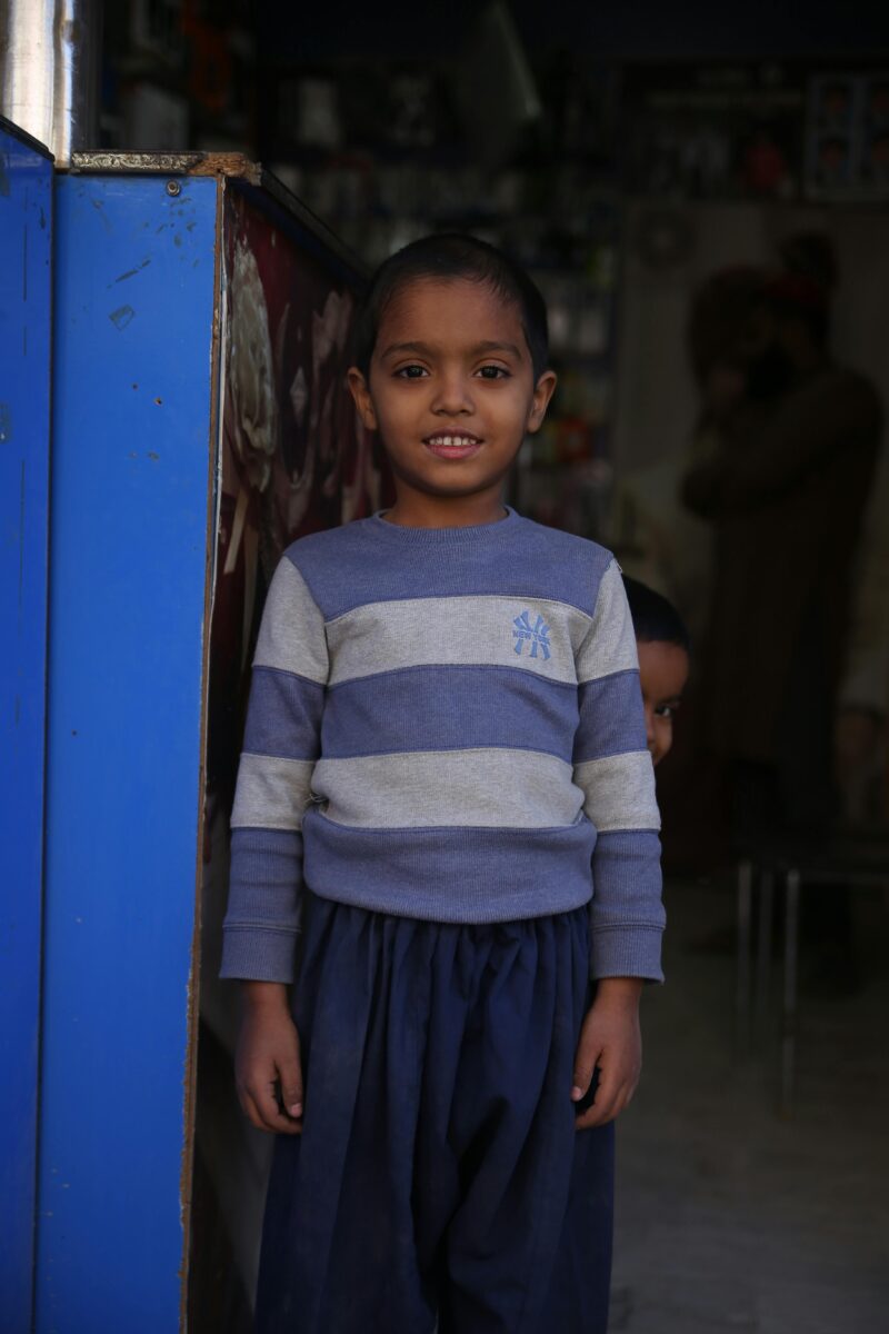pexels-photo-15330517-15330517 A smiling young boy in a striped shirt stands in a casual indoor setting in Karachi, Pakistan.