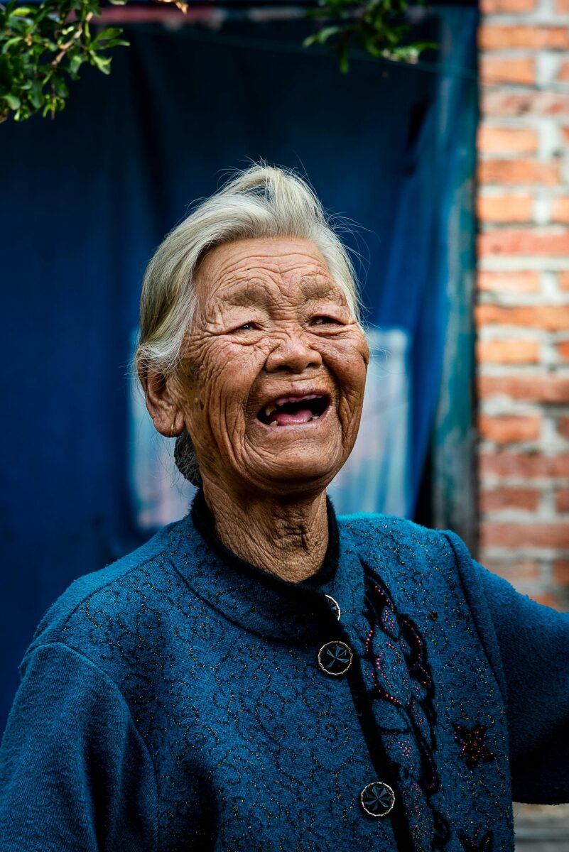 pexels-photo-18377278-18377278 Portrait of a joyful elderly Asian woman smiling outdoors, showcasing happiness and warmth in an outdoor setting.